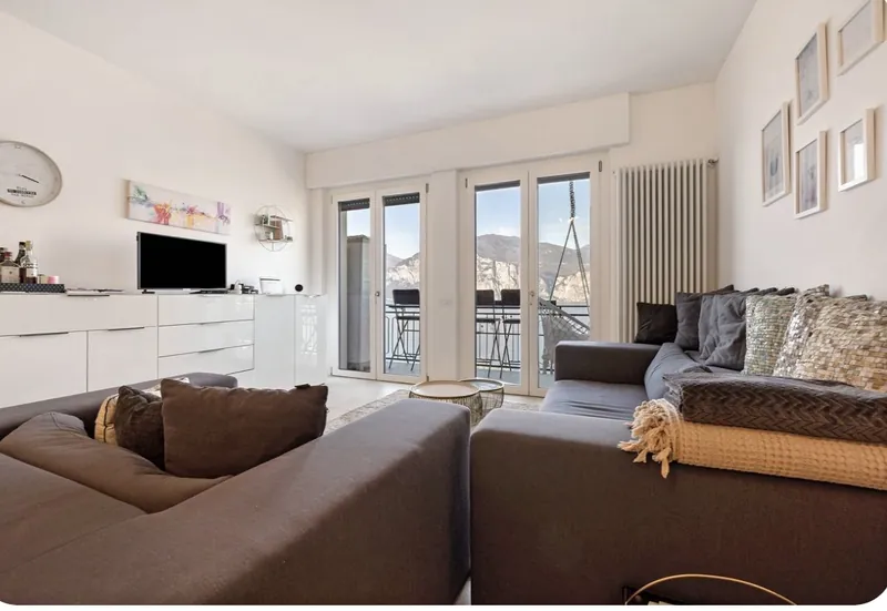 Wohnzimmer mit Ecksofa, TV und Balkontüren zum See